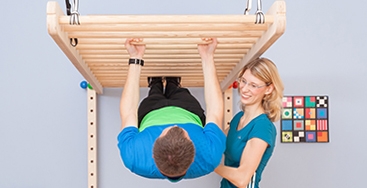 Ariane Hüser unterstützt einen Patienten bei einer Übung an der Hangelstange - Weiterleitung zur Unterseite Rücken-Leistungen